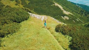 Aerial View Running woman on the top of mountain. Runner is jogging in summer sunny day around trees and mountains background under sun light with blue sky, Drone 4K Video
