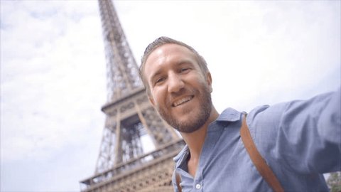 Solo traveller takes selfies under the Eiffel Tower in Paris, France. Young man travelling Europe takes selfies in summer. Slow motion, tourist posing for selfies 