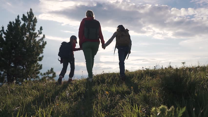Family of tourists on a journey. mother with two daughters in the campaign. children with backpacks admire the view of the mountains. young woman goes with children in the mountains. | Shutterstock HD Video #1013776610