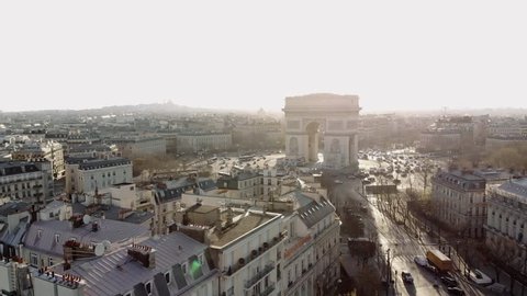Sunny morning in Paris. A wide aerial shot shows the Arc de Triomphe and the Champs Elysees in golden morning light. The camera sinks into a small park in Avenue Foch.