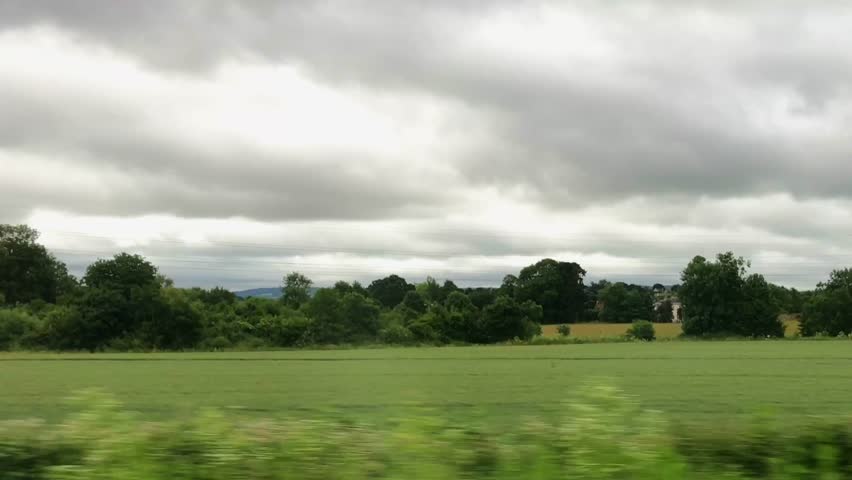 Wide shot out of a window of a moving train, tracking along flat british countryside and farmland