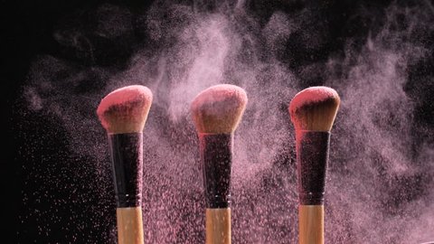 Make-up and beauty concept. Brush with pink powder explosion on black background