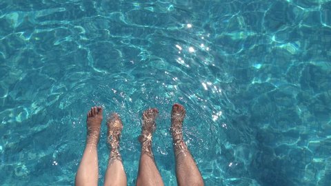 Detail of couple legs relaxing in pool water, romantic summer holiday
