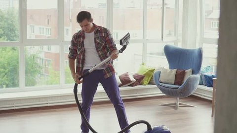 Cheerful man is engaged in cleaning and imagines that he plays the guitar