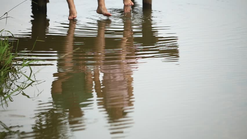 Beautiful youn couple sit on the pier near the lake. make splash by feet. slow motion