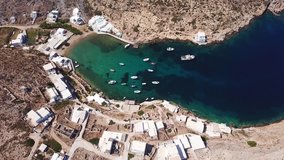 Aerial drone bird's eye view video of picturesque bay and natural fjord of Heronisos with traditional fishing boats, taverns and clear water beach, Sifnos island, Cyclades, Greece
