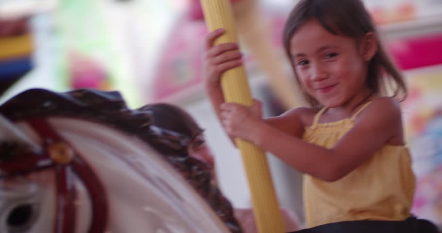 Beautiful little asian girl with mother having fun on merry-go-round ride at funfair