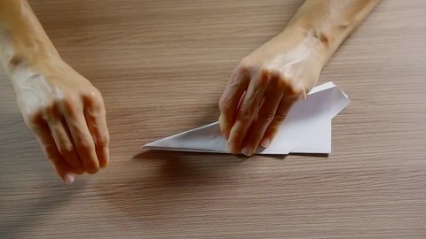 woman is stroking folds of paper origami airplane on a table and throwing it to fly in room
