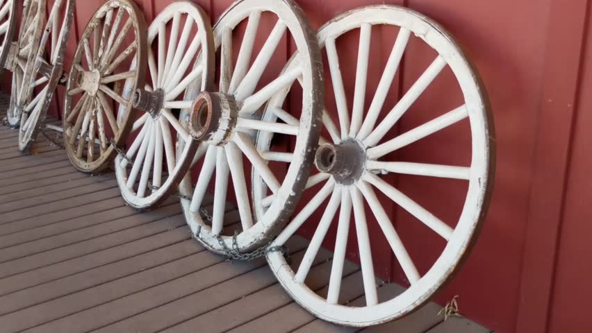 Several old Wooden Wagon wheels all lined up along a wall
