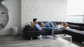 Young hispanic couple laying on couch at home, using a tablet PC for Internet and social media. The boyfriend is giving a massage to feet of the woman. Copy space - Powered by Shutterstock - Get 15% off with code: PIKWIZARD15