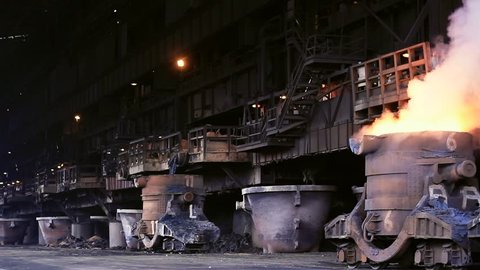 Slow pan of a steel mill blast furnace with smoking crucible filled with molten metal