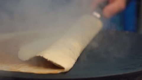 Slow motion of vendor man cooking crepes pancakes in Paris street. Close-up of tasty crepe dessert. Cheff is cooking a pancake made on a metal griddle. The concept of delicious fast food-Dan