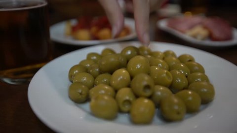 4K, Close up of woman hands holding a green olive in a spanish bar. Typical plate with olives served as tapas. People eating a delicious culinary tapa in Spain-Dan