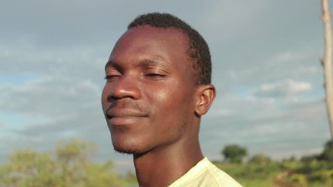 A tight slow motion shot rotating around the face of a hopeful African man in the early morning sun.