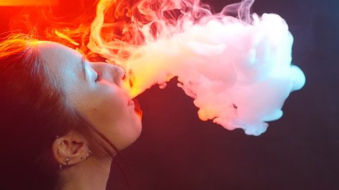Night life concept. Young woman smokes electronic cigarette in color light