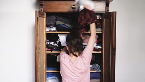 Angry young woman is throwing clothes from old retro vintage wooden wardrobe and after unsuccessful clothes search, view from back, slow motion 1920p HD