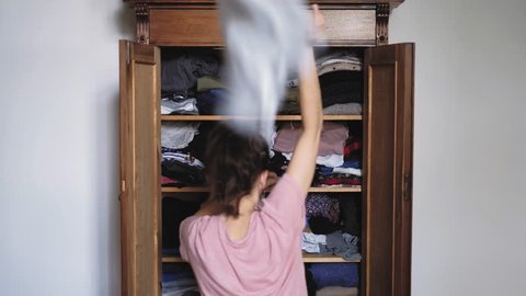 Angry young woman is throwing clothes from old retro vintage wooden wardrobe and after unsuccessful clothes search, view from back, shot in 4K UHD