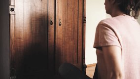 Young girl or woman open old retro vintage wooden wardrobe and search clothes, side view, shot in 4K UHD