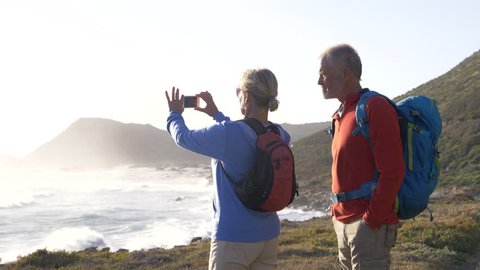 Mature hikers stopping to take photos with a smartphone of the view overlooking the sea