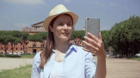 Young woman walking on Circus Maximus and using mobile phone in slow motion in Rome, Italy. Happy female traveler enjoying vacation in european city. Smiling girl having video chat via online app