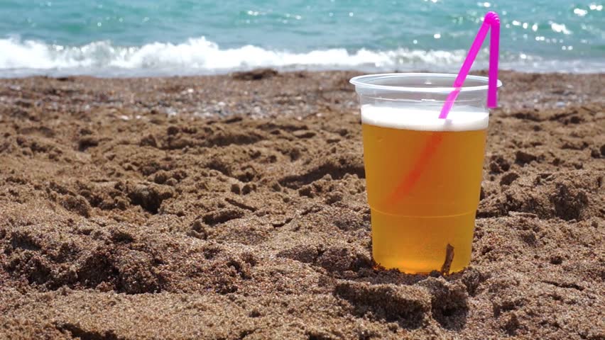 Plastic glass of cold beer on a background of the blurred sea.