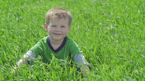 View of a smiling boy sitting in a green field.