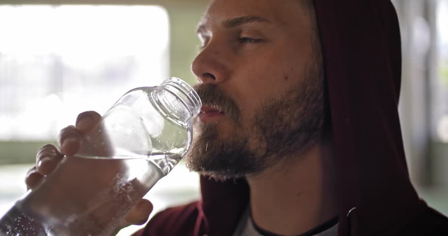 Young adult man with hooded sweatshirt drinking water resting during fitness sport workout .Grunge industrial urban training.4k slow motion video | Shutterstock HD Video #1013866049
