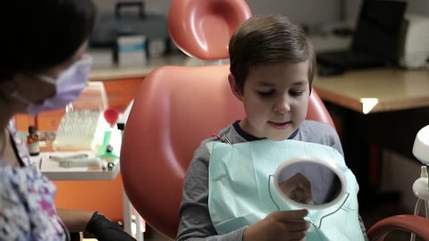 medicine, dentistry and healthcare concept - female dentist with kid patient at dental clinic adjusting chair