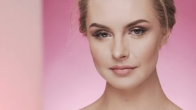 Beauty video concept, close up portrait at pink background, smiling and looking at camera
