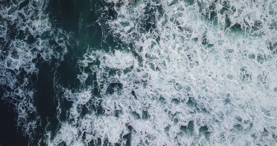 Aerial top view waves break on dark rocks near beach. Sea waves on the dangerous stones aerial view drone 4k shot. Bird's eye view of ocean waves crashing against an empty beach from above. Royalty-Free Stock Footage #1013883026