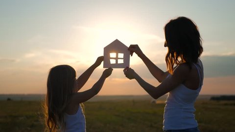 Silhouette happy mother and daughter with dream house. Paper house as a symbol. The concept of family happiness.
