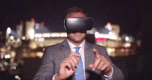 Young business man wearing VR headset at night typing on virtual screen with city downtown lights in background