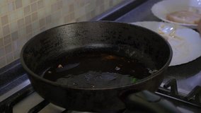 Frying pan with hot oil. The man puts the pieces of fish fillet into it.