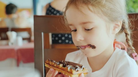 The little sweetheart was all smeared with chocolate, the child is sitting in a restaurant and eating chocolate cake Video de stock