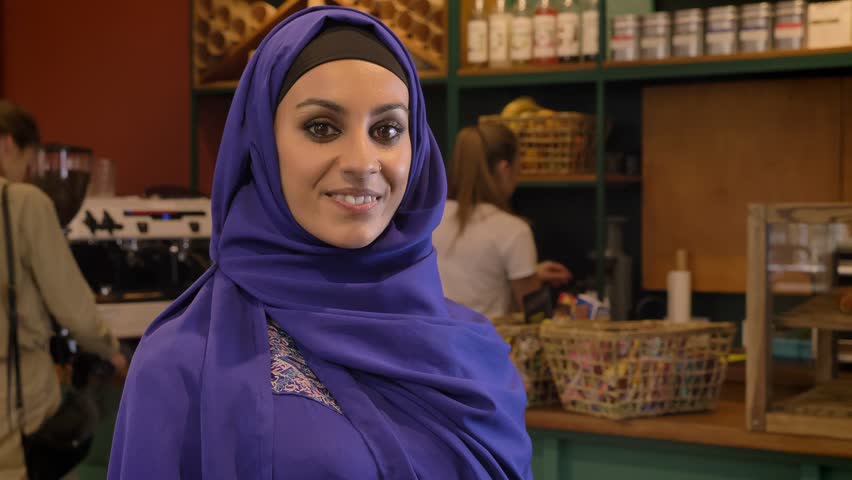 Portrait of young muslim woman in hijab standing in cafe and smiling at camera, charming lady with pierced nose