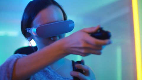 Pro Gamer Girl Wearing Virtual Reality Headset Plays Online Video Game with Joysticks / Controllers. Cool Retro Neon Colors in the Room. Shot on RED EPIC-W 8K Helium Cinema Camera.