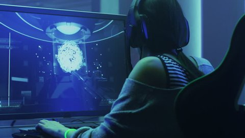 Beautiful Professional Gamer Girl Playing in First-Person Shooter Online Video Game on Her Personal Computer. Casual Cute Geek Girl Wearing Headset. Shot on RED EPIC-W 8K Helium Cinema Camera.