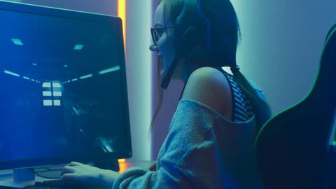 Beautiful Professional Gamer Girl Playing in First-Person Shooter Online Video Game on Her Personal Computer. Casual Cute Geek Girl Wearing Headset. Shot on RED EPIC-W 8K Helium Cinema Camera.