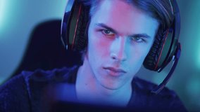 Portrait of the Young Handsome Pro Gamer Playing in Online Video Game, talks with Team Players through Microphone. Neon Colored Room. Shot on RED EPIC-W 8K Helium Cinema Camera.