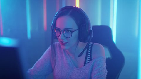 Beautiful Professional Gamer Girl Sitting Down to Playing in Online Video Game on Her Personal Computer. Casual Cute Geek wearing Glasses and Talking into Microphone.  Shot on RED EPIC-W 8K.