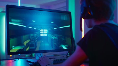 Pro Gamer Playing in First-Person Shooter Online Video Game on His Personal Computer, He Wins Tournament and Celebrates. Room Lit by Neon Lights in Retro Arcade Style. Shot on RED EPIC-W 8K Camera.