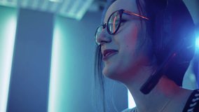 Low Angle Portrait Shot of the Beautiful Pro Gamer Girl Playing in Online Video Game, Cute Geek Girl in Glasses, talks with Team Players through Microphone. Neon Colored Room. Shot on RED EPIC-W 8K