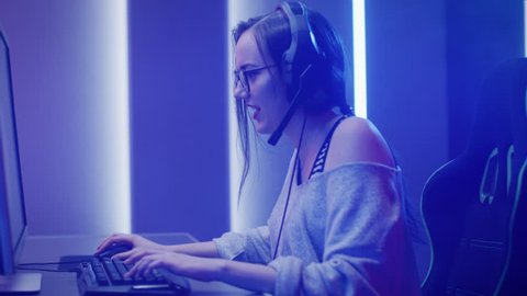 Arc Shot of the Beautiful Pro Gamer Girl Playing in First-Person Shooter Online Video Game on Her Personal Computer. Casual Cute Geek wearing Glasses and Headset. Neon Room.  Shot on RED EPIC-W 8K.