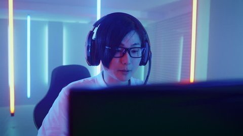 Professional East Asian Gamer Playing in Online Video Game on His Personal Computer. Talks with His Team Through Microphone. Shot on RED EPIC-W 8K Helium Cinema Camera.