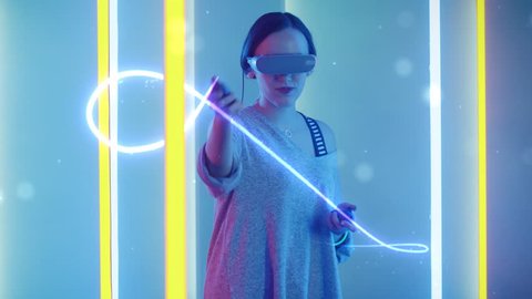 Beautiful Young Girl Wearing Virtual Reality Headset Draws Abstract Lines and Figures with Joysticks  Controllers. Creative Young Girl Does Concept Art with Augmented Reality. Shot on RED EPIC-W 8K.