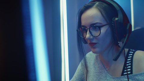 Close-up Portrait of the Beautiful Professional Gamer Girl Playing in Online Video Game, Casual Cute Geek wearing Glasses, talks/ chats with Her Friends through Headset.  Shot on RED EPIC-W 8K Camera.