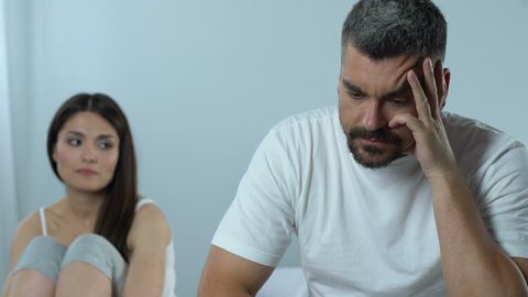 Upset man and supportive wife sitting in bedroom, impotence, family crisis