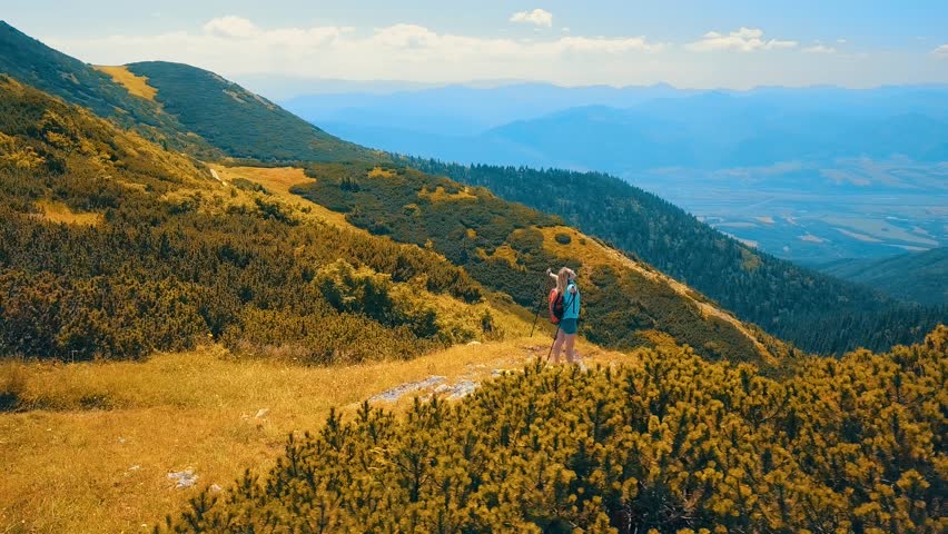 Aerial View Happiness Woman tourist walking on the top of mountain in summer sunny day under sun light. Beautiful mountains landscape view. Drone 4K Video.