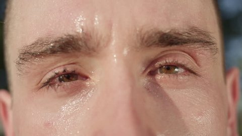 SLOW MOTION, CLOSE UP, MACRO, DOF: Unknown adult male's eyes after a tough workout in the sunny nature. Unrecognizable sweaty Caucasian man looking around park after exercising on a hot summer day.