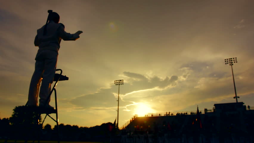 Silhouetted marching band preforming before a high school football game.